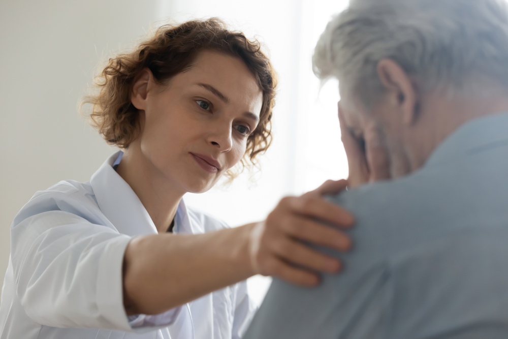 Head shot close up compassionate young general practitioner doctor supporting desperate stressed older mature retired man at appointment. Medical kindness, psychological help, soothing concept.